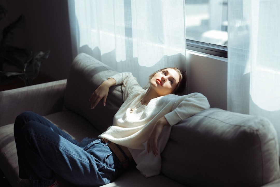 A woman in a white sweater and blue jeans reclining on a grey sofa