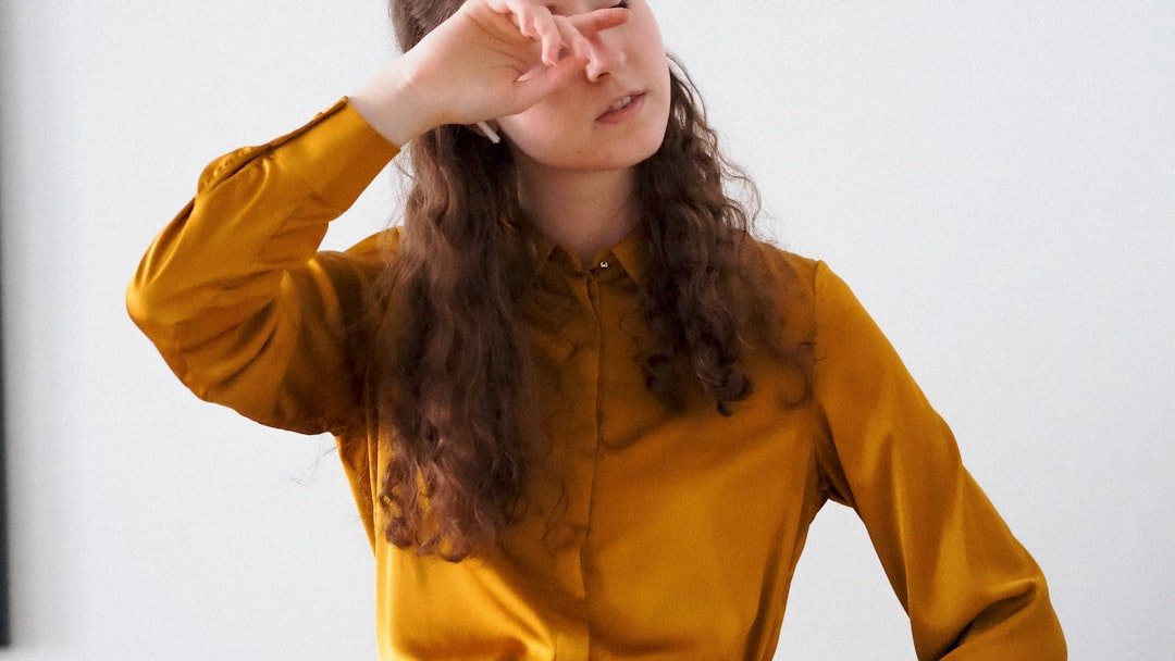 A woman in a yellow shirt is holding her hand up to her face
