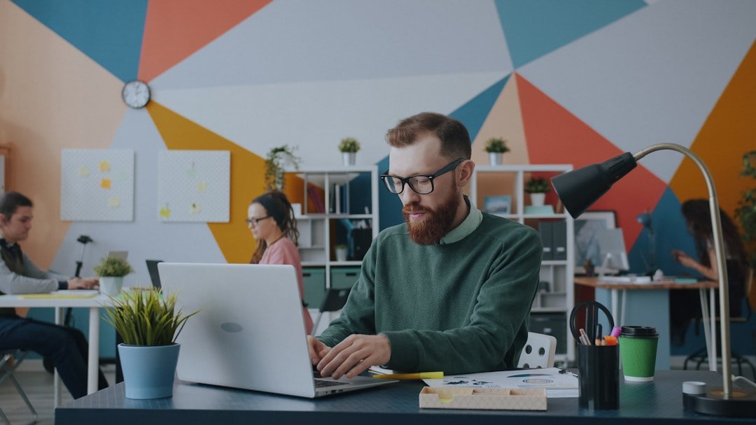Office noise: A man with a beard and glasses typing on a laptop in a colorful office