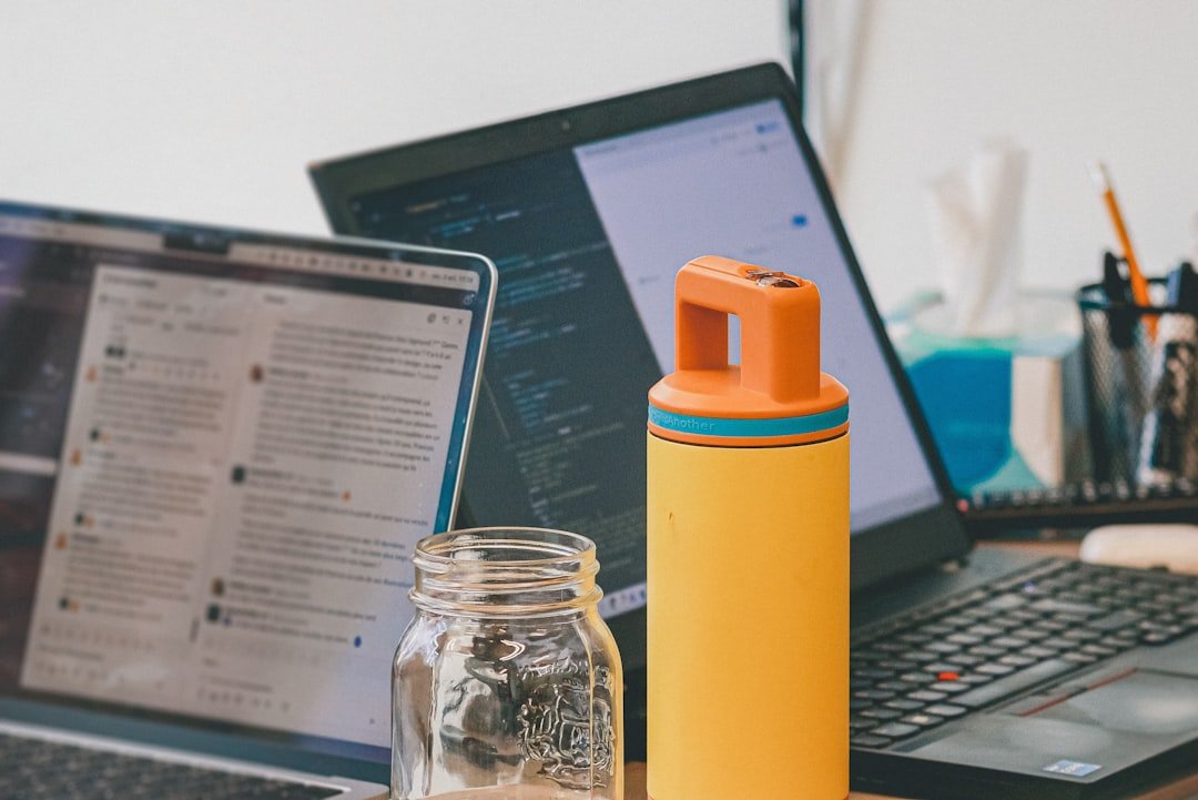 Two laptops and a yellow water bottle on desk