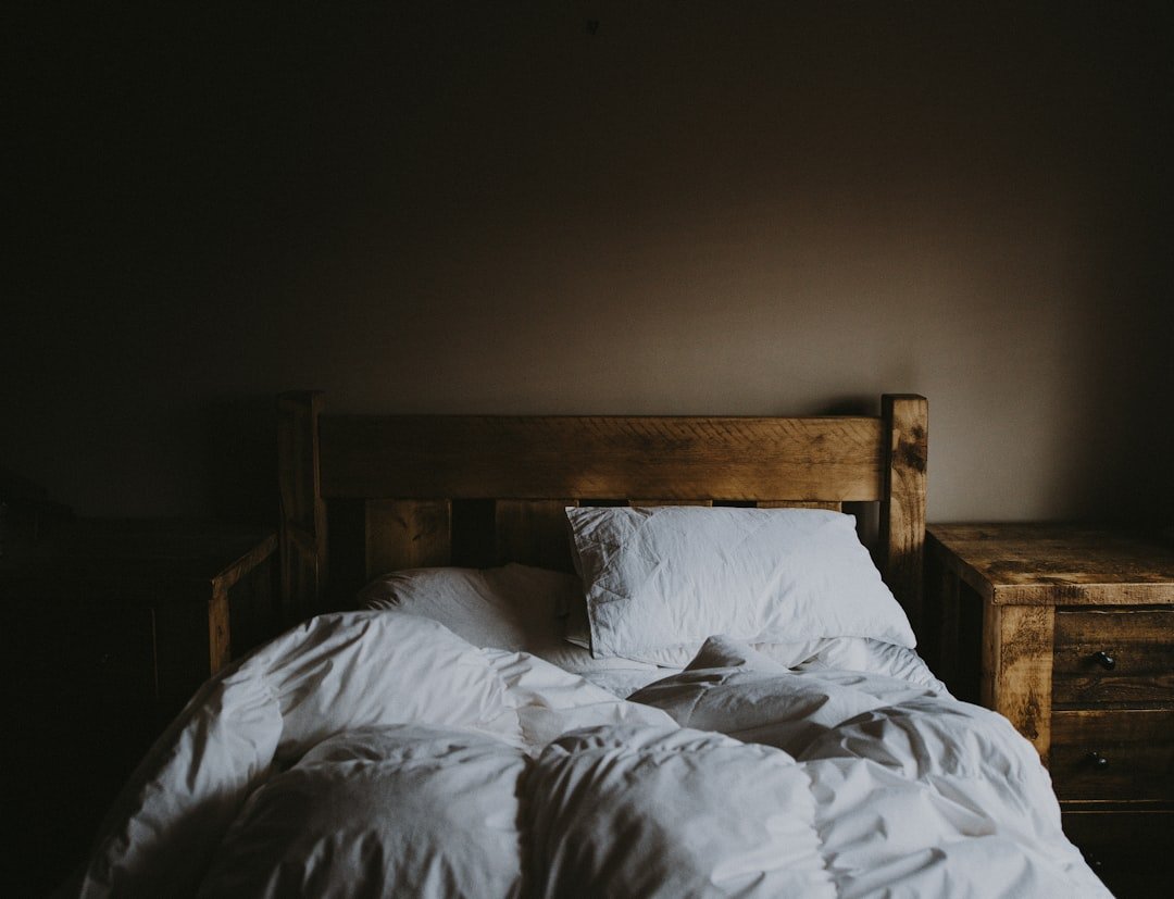 White bed comforter set and brown wooden bed frame beside brown wooden nightstand
