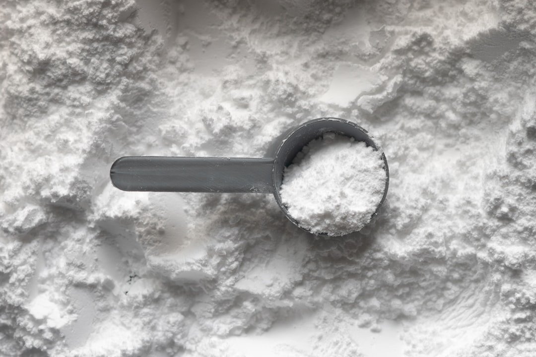 Creatine: A grey plastic scoop filled with white powder resting on a pile of powder