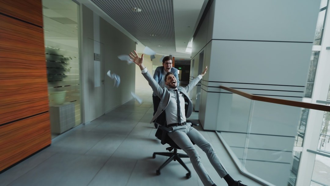 Man in suit rides office chair pushed by colleague