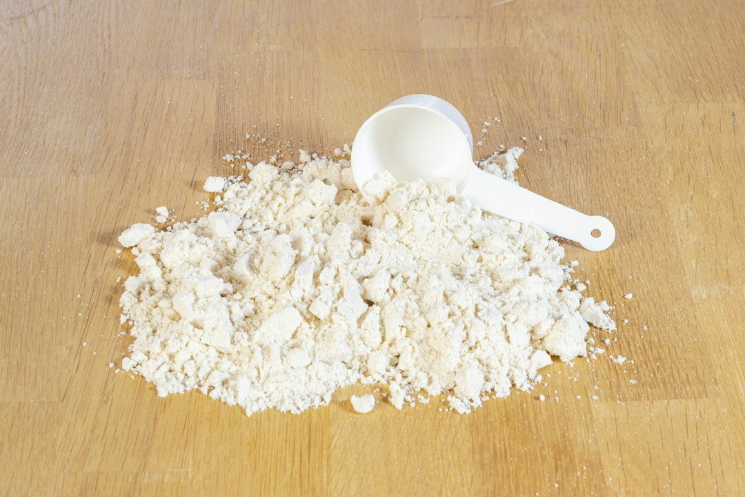 A scoop of protein powder on a wooden surface