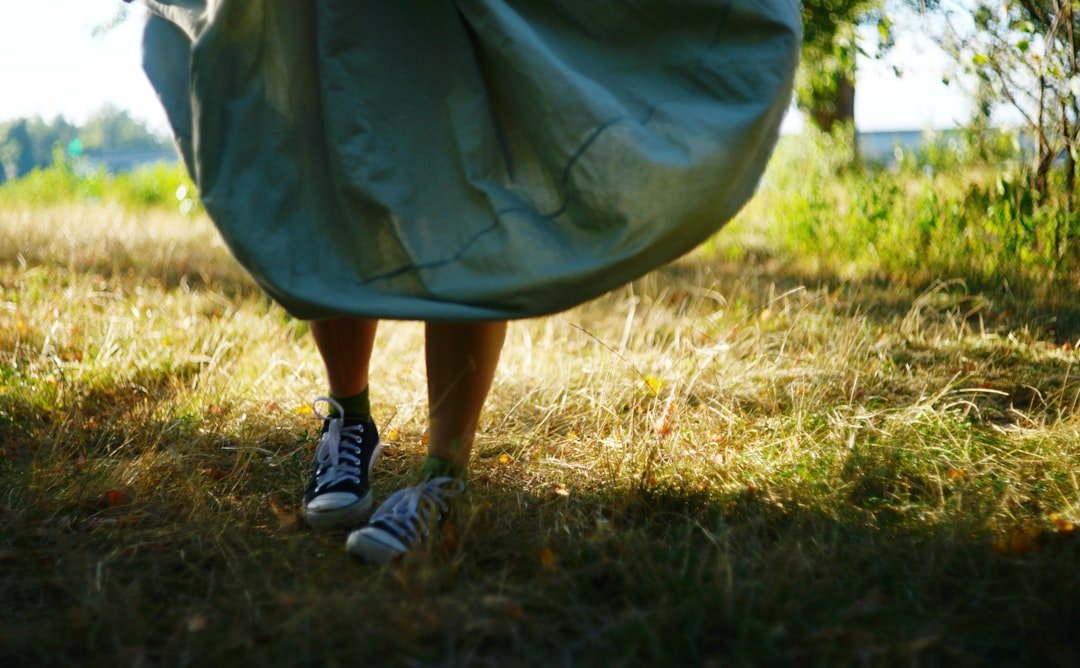 A person in a flowing skirt and sneakers walking through a sunlit field