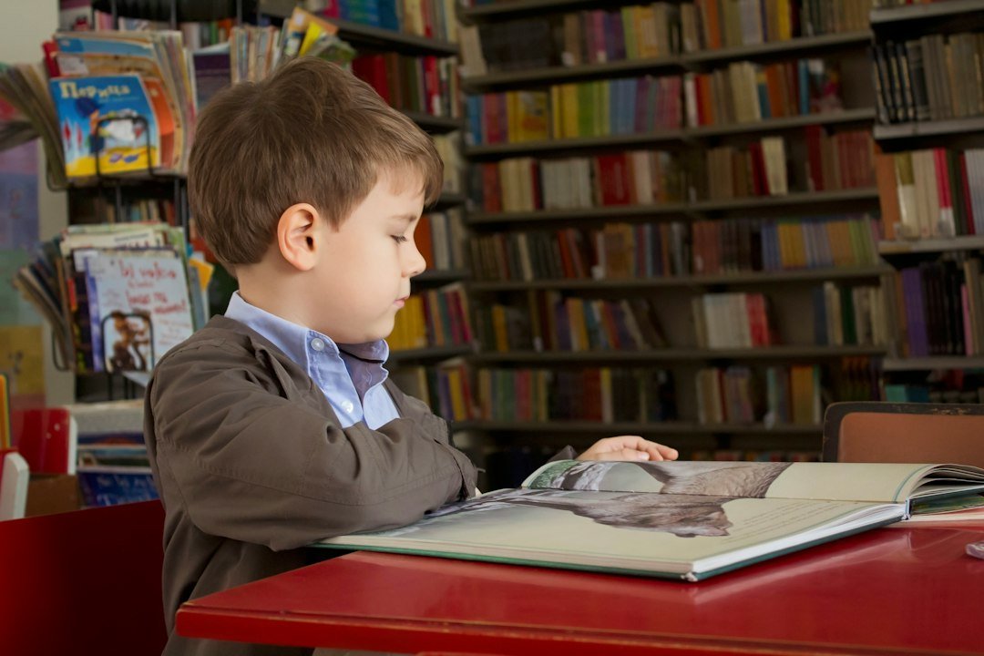 Boy sitting near red table reading book
