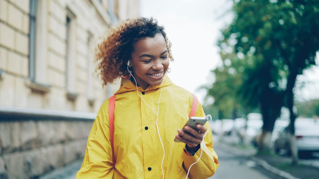 Young woman in yellow raincoat listening to music outdoors
