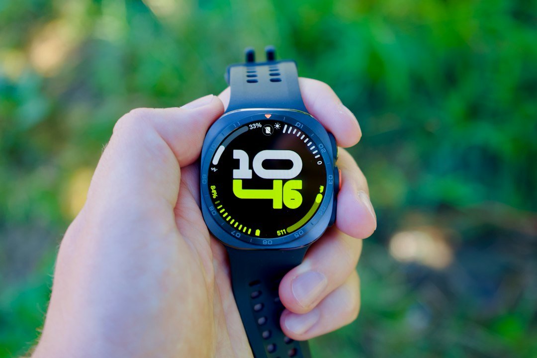A hand holding a black smartwatch with a digital clock face against green foliage