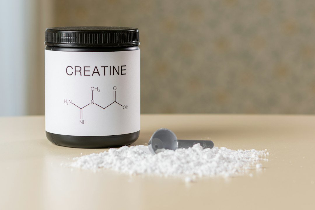 A bottle of creatine next to a spoon on a table